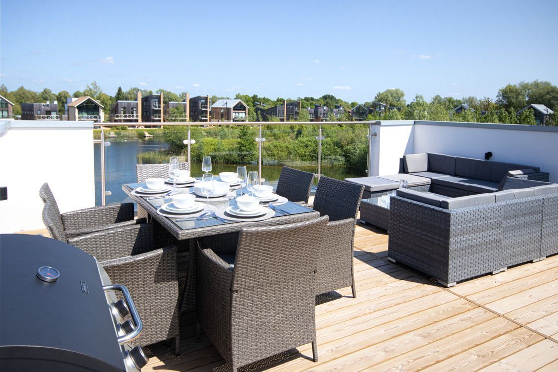 Una terraza en la azotea con una mesa de comedor preparada para cuatro personas, rodeada de sillas de mimbre y una parrilla.