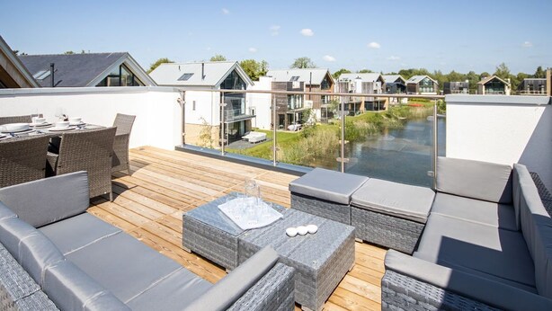 Terraza en la azotea con mobiliario exterior, barandilla de cristal y vistas a casas vecinas.
