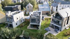 Un área residencial moderna con casas contemporáneas, incluyendo una casa de dos plantas con balcón y una casa de techo plano con un automóvil estacionado frente.
