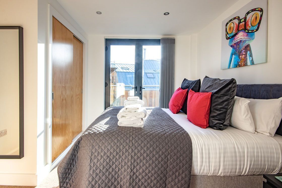 Habitación de hotel con una cama grande, vista a través de una puerta corredera y un cuadro llamativo en la pared.