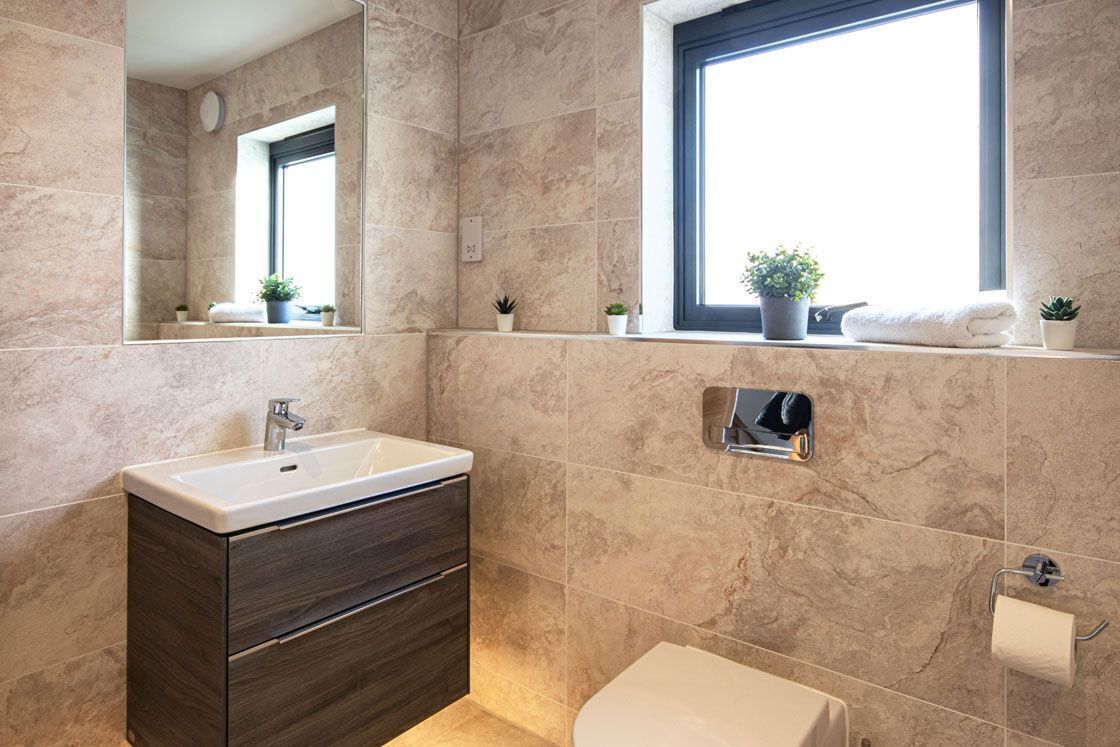 A modern bathroom with a large mirror, a sink, a toilet, and a window with plants on the windowsill.