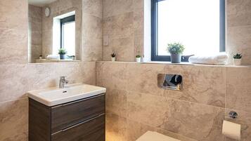 A modern bathroom with a large mirror, a sink, a toilet, and a window with plants on the windowsill.