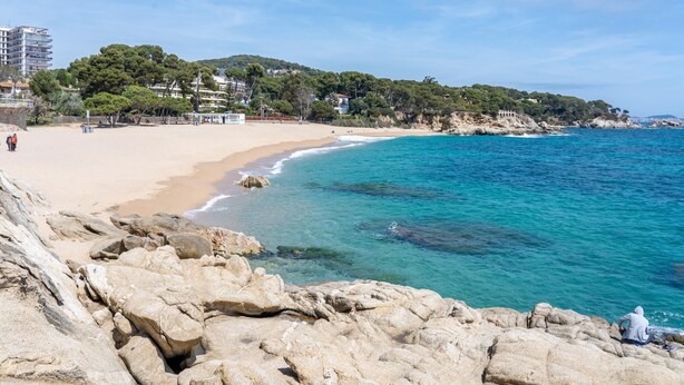 A coastal beach with clear turquoise waters, rocky shoreline, and buildings in the background. - Perfect space in Platja d'Aro, Costa Brava (Platja d'Aro)