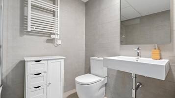 A modern bathroom with a white toilet, a white sink with a wooden soap dispenser, and a cabinet with drawers.
