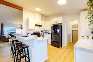 A modern kitchen with white cabinets, a central island with stools, stainless steel appliances, and a wooden floor.