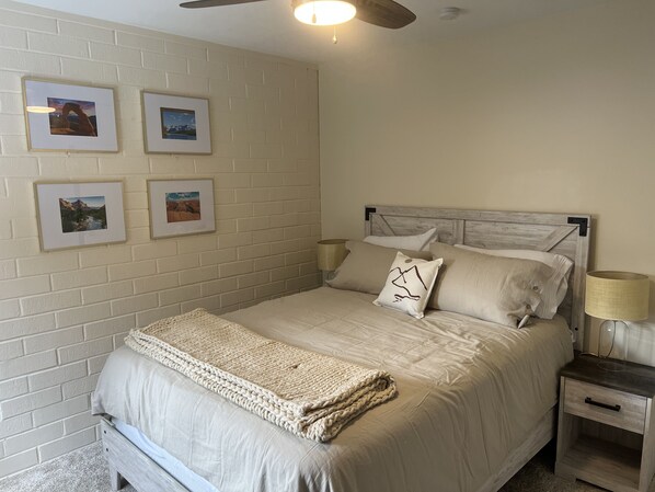A bedroom with a bed, a nightstand, a lamp, and four framed pictures on the wall.