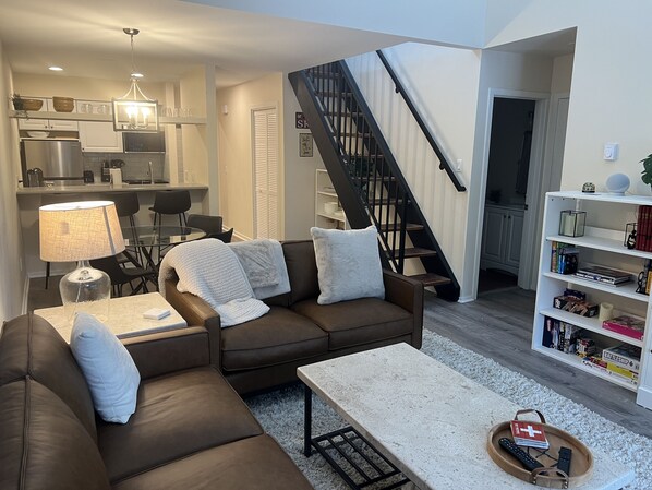 A modern living room with a brown leather sofa, a coffee table, and a bookshelf. A staircase leads to an upper level. - 2 bedroom + loft w/AC close to it all!! (Park City)