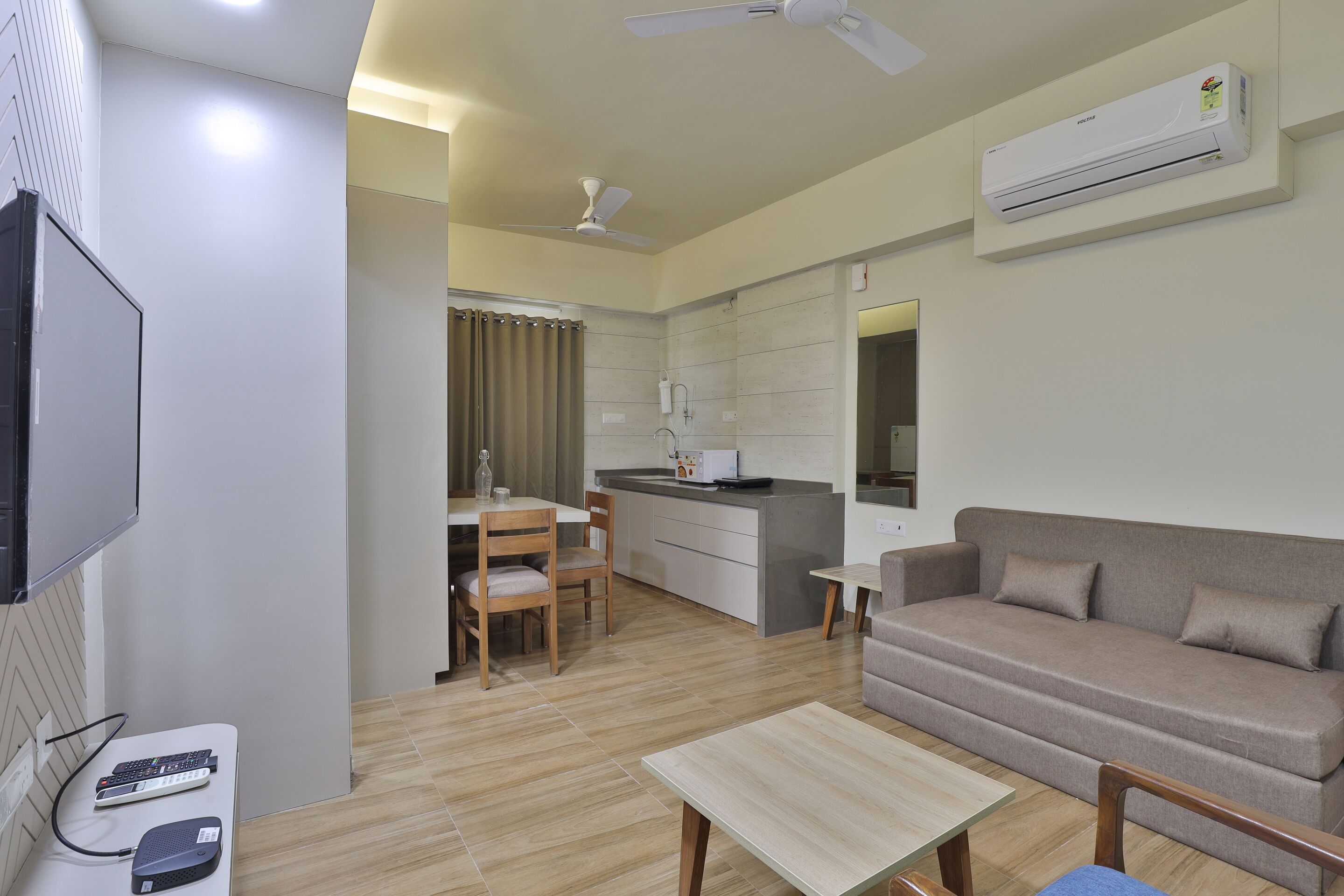 A modern living room with a sofa, a coffee table, and a TV. There is a kitchen area with a dining table and chairs.