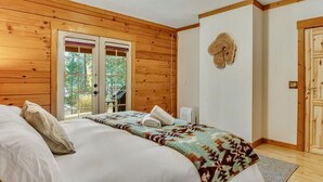 A bedroom with a wooden ceiling and walls, a bed with white linens, a patterned throw blanket, and a door with a wooden frame.