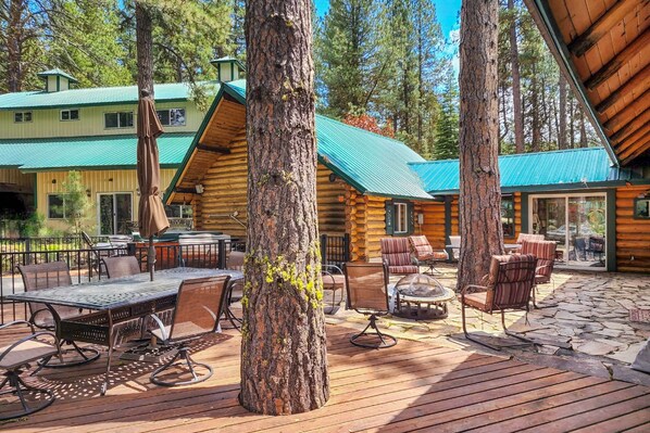 A wooden cabin with a deck, outdoor seating, and a large tree in the center.