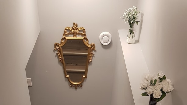 A staircase with wooden steps and white railings, a decorative gold-framed mirror, and a vase with white flowers. - Pleasant 1 Bedroom Private Suite in the Meadows (Saskatoon)