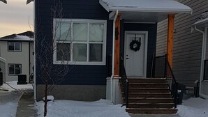 A two-story house with a porch, a front door with a wreath, and a staircase leading to the entrance. - Pleasant 1 Bedroom Private Suite in the Meadows (Saskatoon)