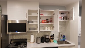 A modern kitchen with white cabinets, a stainless steel microwave, a built-in oven, a sink, and various kitchen appliances. - Pleasant 1 Bedroom Private Suite in the Meadows (Saskatoon)