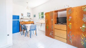 A compact kitchen with a dining area, featuring a wooden cabinet with floral designs, a refrigerator, and a dining table with chairs.