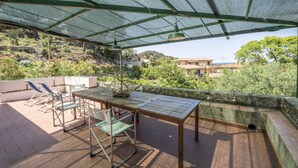 An outdoor patio with a table and chairs, a hanging lamp, and a view of a hillside with buildings.