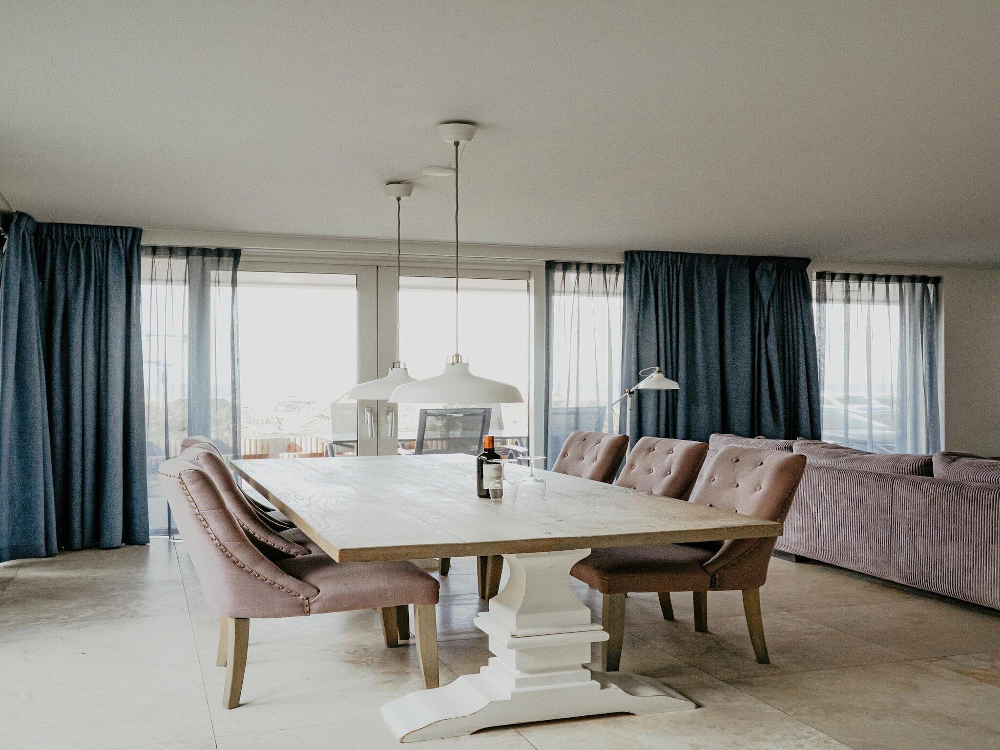 A spacious dining area with a long wooden table, cushioned chairs, and pendant lighting.
