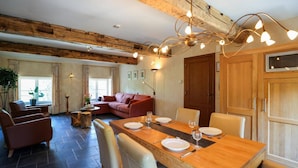 Een eetgedeelte met een houten tafel voor vier personen, omringd door stoelen, in een kamer met zichtbare houten balken en een groot raam.