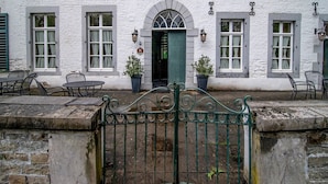 Een wit gebouw met een groene deur, meerdere ramen en terrasplekken.