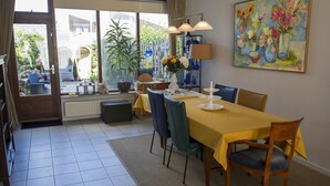 Een eetruimte met een gele tafel, stoelen, een lamp en een schilderij aan de muur.