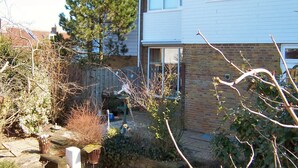 Een woonhuis met bakstenen gevel, een houten terras en een tuin met verschillende planten en een vogelhuis.