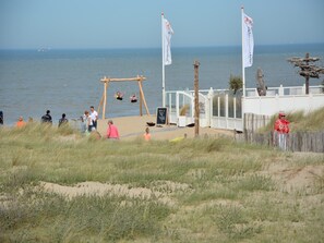A beach with a swing set, a wooden fence, and flags. - Holiday Home Noordwijk near Beach (Noordwijk)