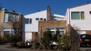 Een woonwijk met huizen, waaronder een wit huis met een bakstenen gedeelte en een garage, met een auto ervoor geparkeerd.