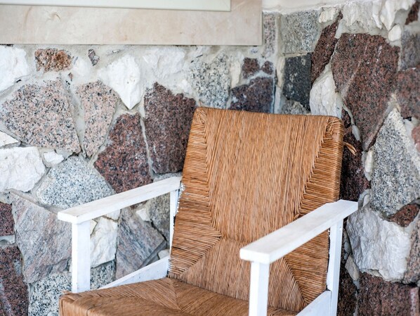 A wicker chair with white armrests against a stone wall.