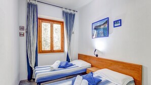 A room with two beds, a window with curtains, a nightstand, and two framed pictures on the wall.