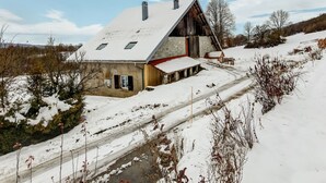 Ein schneebedecktes Landhaus mit geneigtem Dach, Schornstein und einem kleinen angebauten Schuppen.