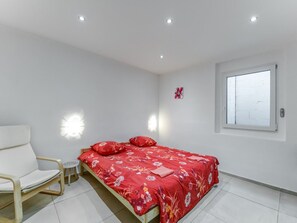 Een slaapkamer met een bed, een stoel, een klein tafeltje en een raam.