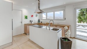 Eine moderne Küche mit einer zentralen Kochinsel, Edelstahlgeräten und Blick auf eine verschneite Landschaft durch große Fenster.