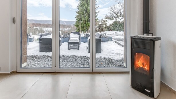 Ein Zimmer mit Glastür, das zu einem verschneiten Außenbereich mit Sitzgelegenheit und Kamin führt.