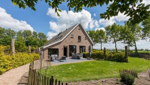 Une ferme en briques avec une grande terrasse, un espace salon extérieur et un jardin bien entretenu.