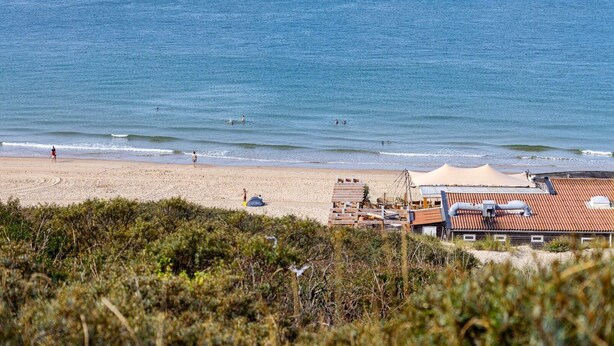 A beach with a sandy shore, a few people, and a building with a red roof in the foreground. - Apartment in Koudekerke near Seabeach (Dishoek)
