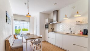 A modern kitchen with white cabinets, a wooden dining table, and pendant lighting. - Apartment in Koudekerke near Seabeach (Dishoek)