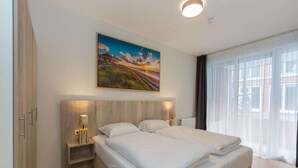 Ein modernes Hotelzimmer mit einem großen Bett, Nachttischen mit Lampen, einem Bild an der Wand und einem großen Fenster mit Vorhängen.