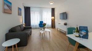 Ein modernes Wohnzimmer mit einem grauen Sofa, einem kleinen weißen Tisch, einem blauen Sessel, einer weißen Kommode und einem an der Wand montierten Fernseher.