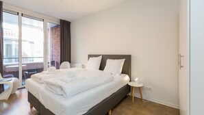 A modern hotel room with a large bed, a small bedside table, and a view of the city through large windows.