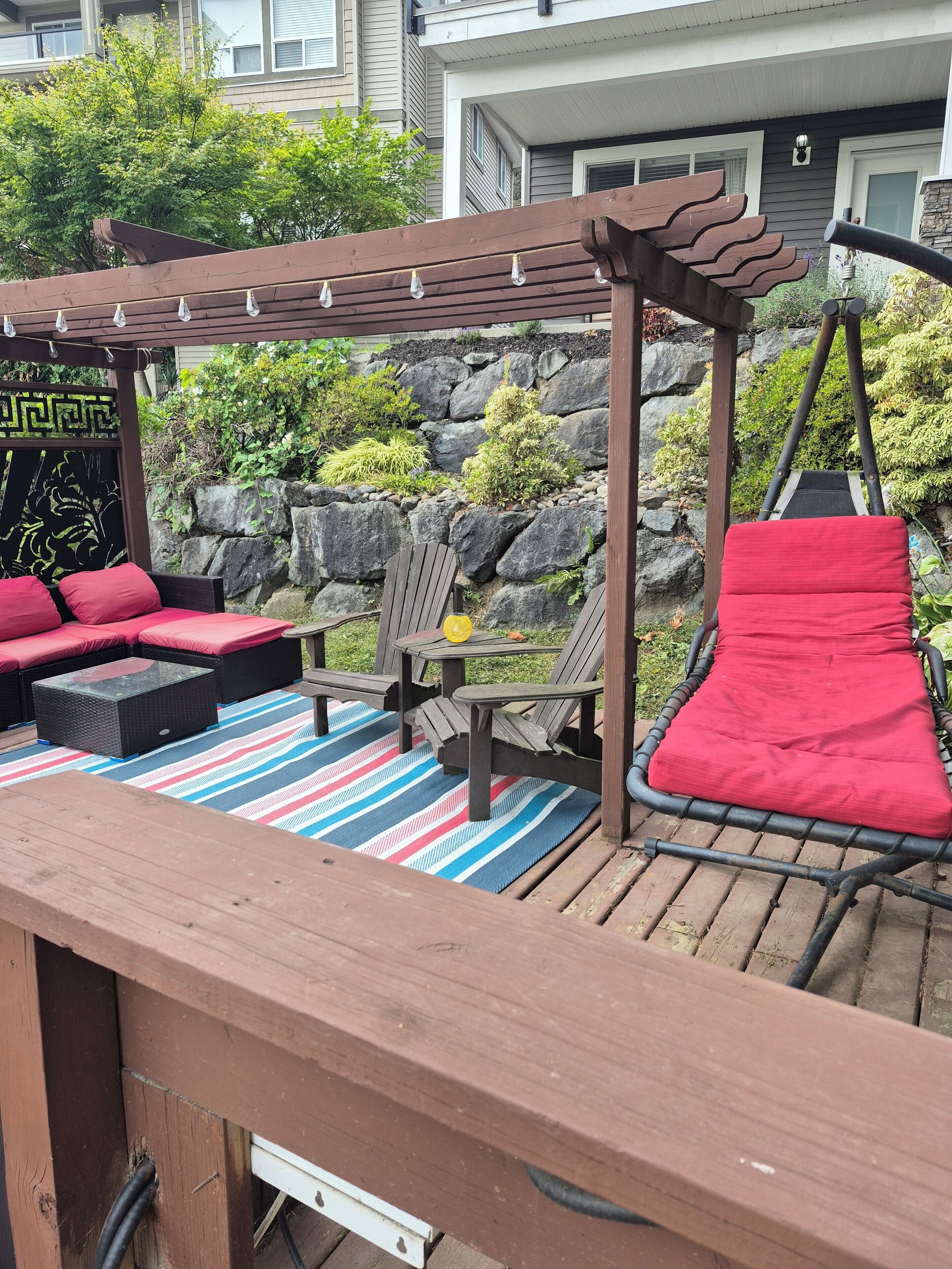 A wooden deck with outdoor seating, including a sofa and chairs, and a swing set.