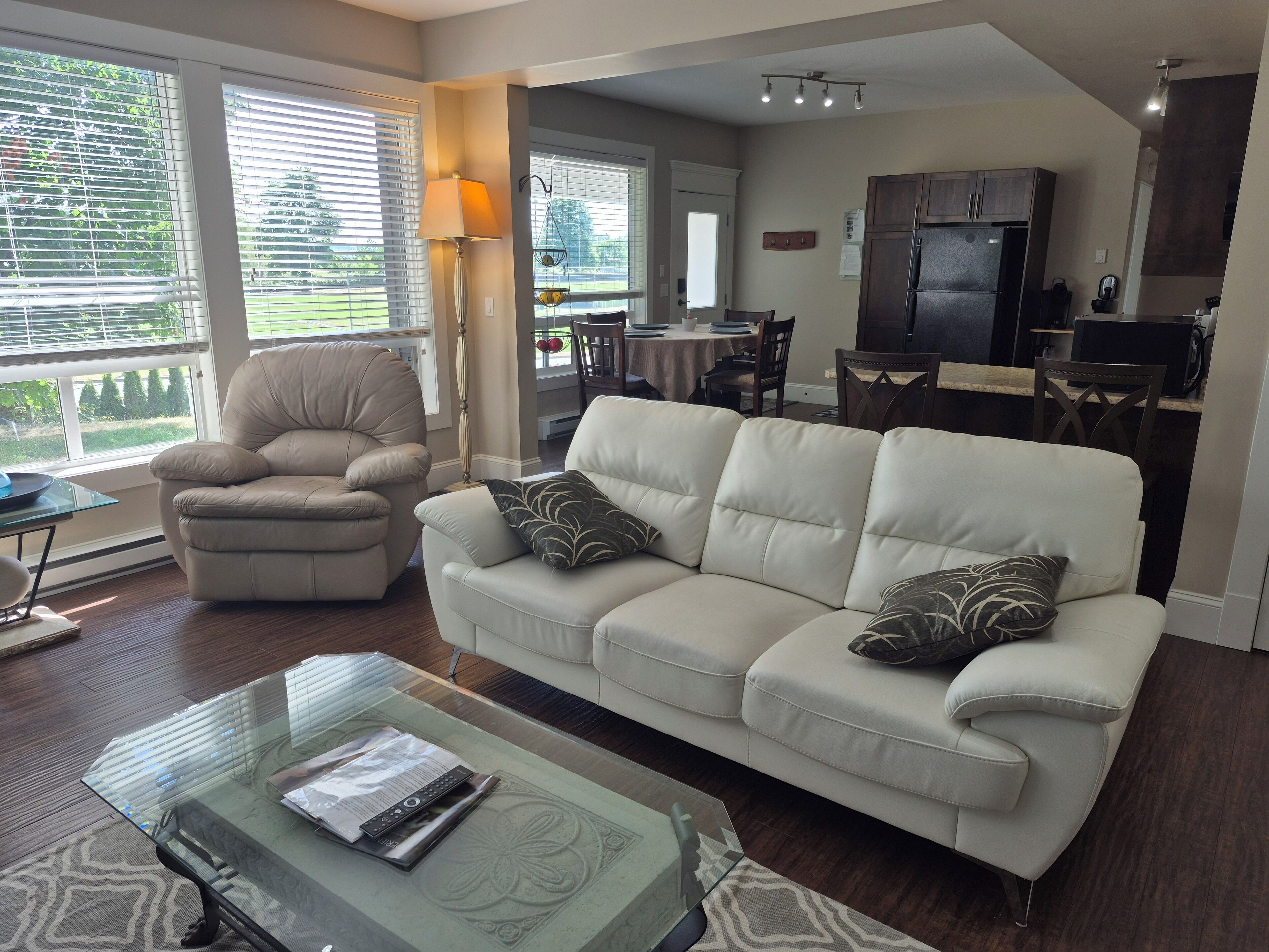 A modern living room with a beige sofa, a glass coffee table, and a dining area in the background.