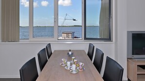 Een eethoek met een grote tafel, vier stoelen en uitzicht op een meer met een kraan.