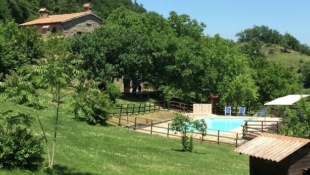 Zona de piscina rodeada de vegetación exuberante y un edificio de piedra.
