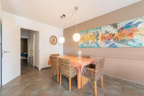 Un coin repas avec une table en bois et des chaises en osier, une grande peinture abstraite au mur et une horloge.