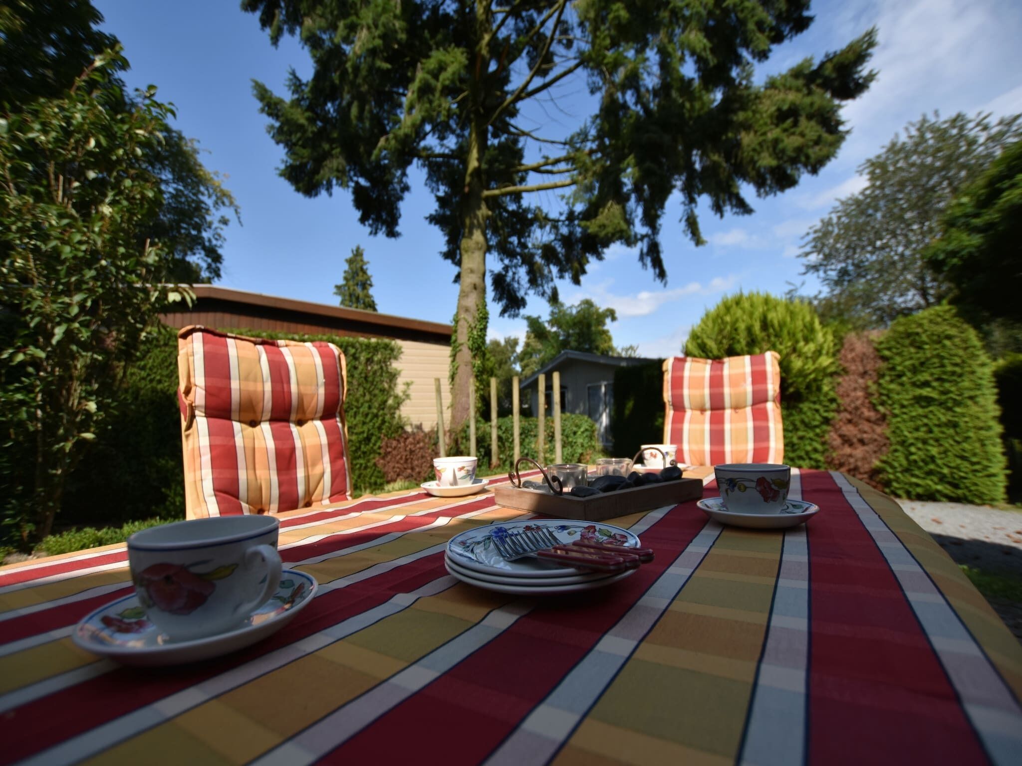 Un área de comedor al aire libre con cojines a rayas, una mesa dispuesta con platos, vasos y una bandeja de comida.