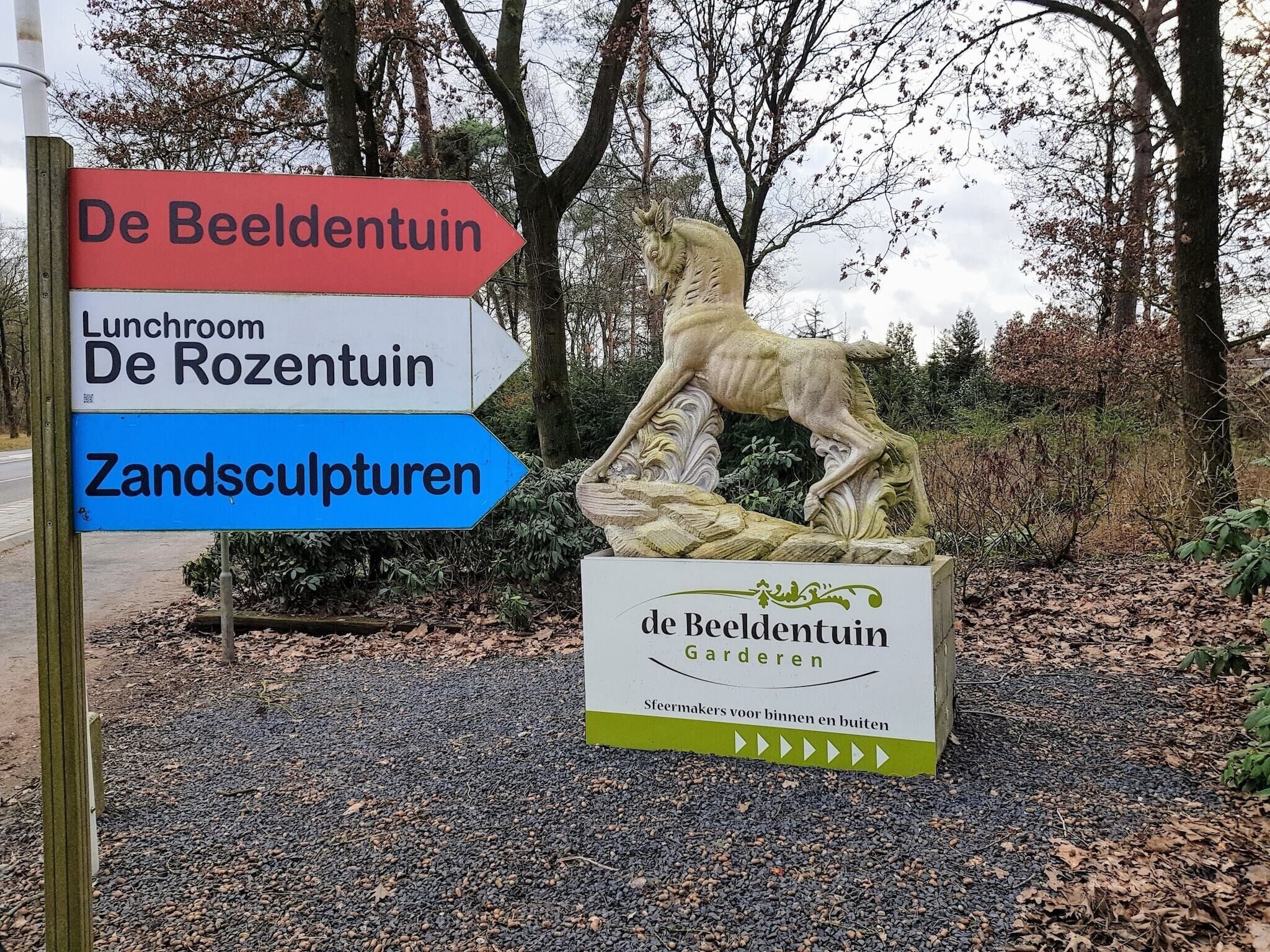 Un panneau indicateur indiquant la direction du jardin de sculptures (De Beeldentuin), du jardin de roses (De Rozentuin) et des sculptures de sable (Zandsculpturen).
