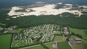 Vue aérienne d’un quartier résidentiel avec une vaste étendue d’eau, des champs verdoyants et une forêt dense.