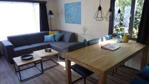 A modern living room with a sofa, a dining table, and a coffee table. There is a painting on the wall and a window with curtains. - Chalet near Loonse and Drunense Duinen (Udenhout)