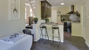 A modern kitchen with a central island, bar stools, and a dining area with a white table and chairs. - Villa in Netherlands with Sauna & Comfort (Uden)