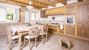 A rustic kitchen with wooden beams, a dining table with chairs, and a small window.