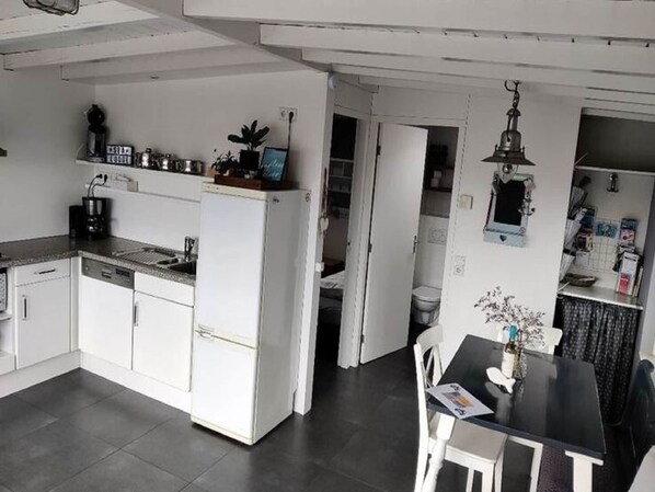 A compact kitchen with white cabinets, a refrigerator, a coffee maker, and a dining area with a table and chairs.